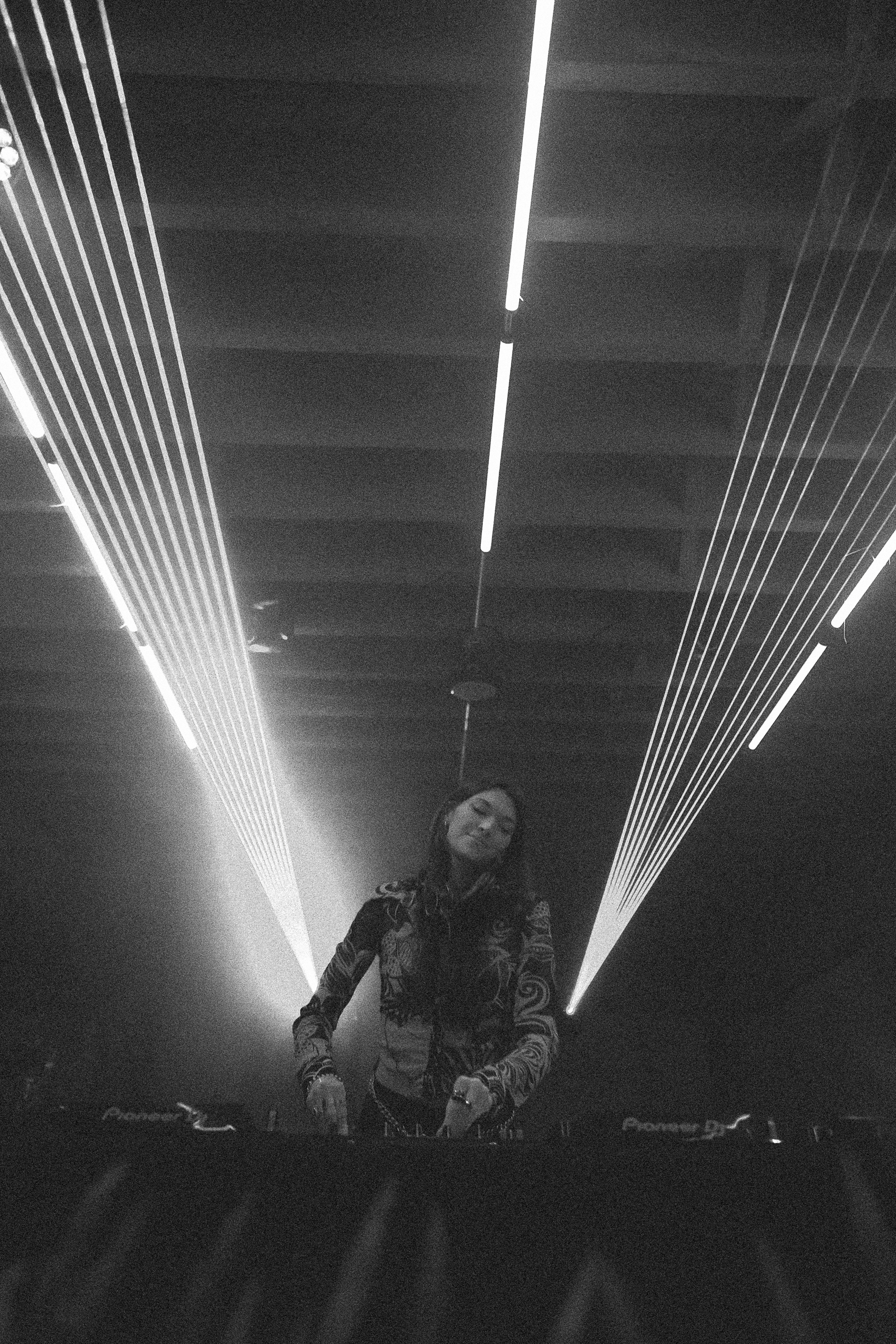 A DJ playing beneath monochrome laser beams